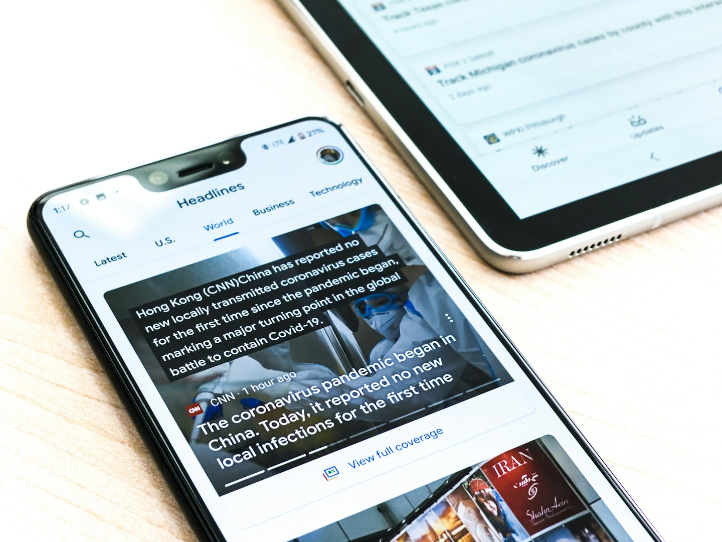 Smartphone y tablet mostrando aplicaciones de noticias sobre un escritorio de madera.