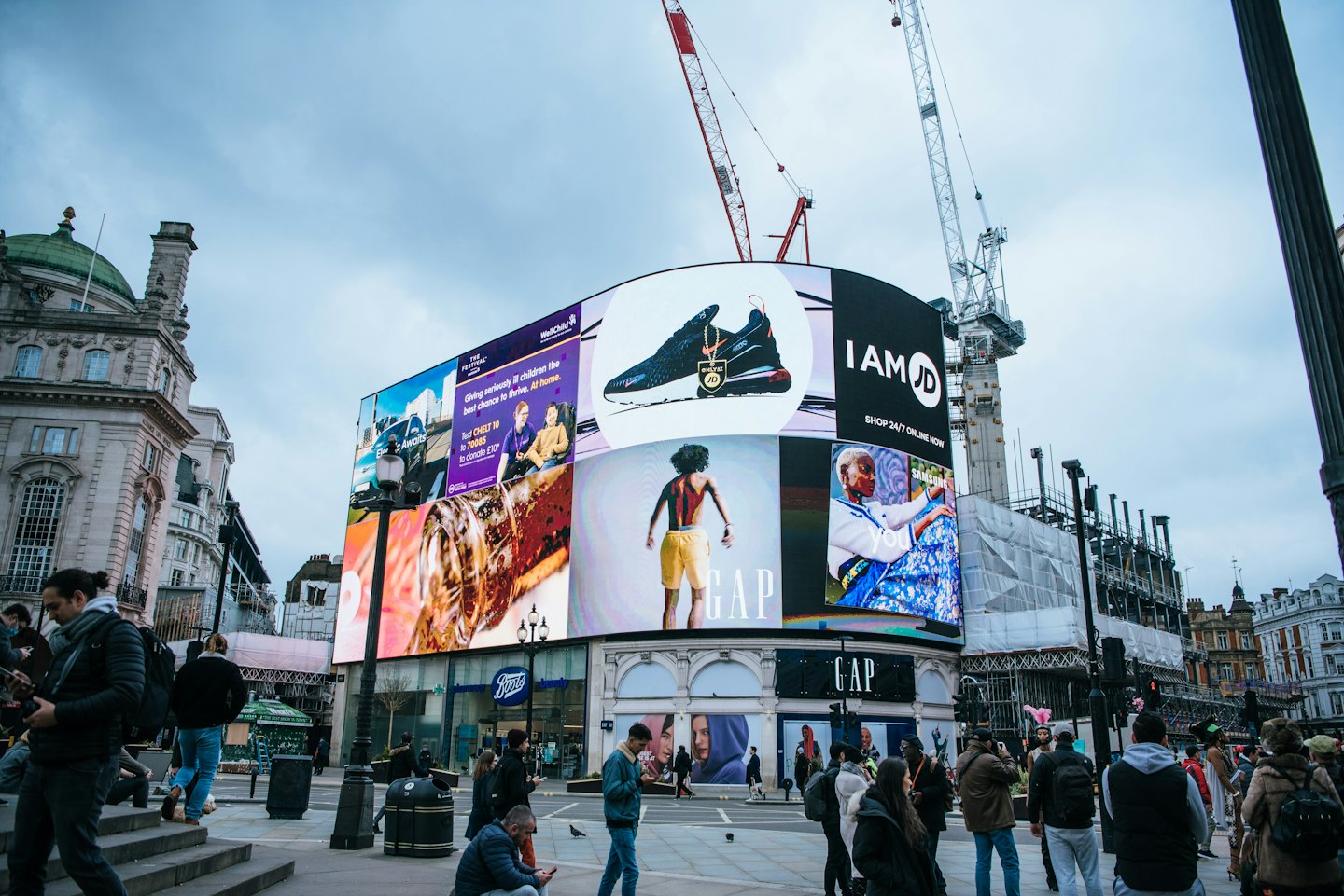 Gente paseando por una plaza de ciudad concurrida con una gran pantalla LED.