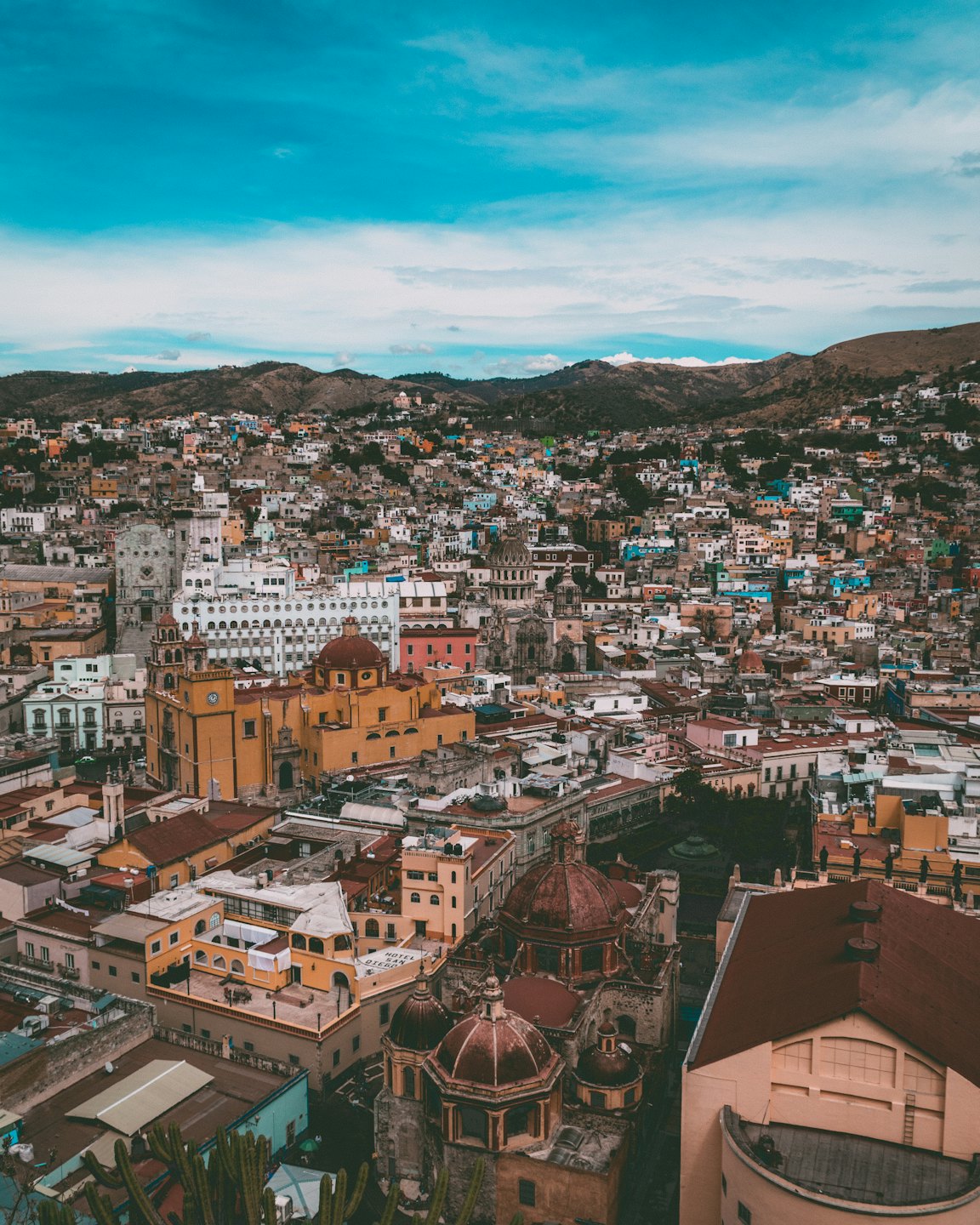 Edificios coloniales coloridos con tejados rojos en un valle bajo colinas áridas.